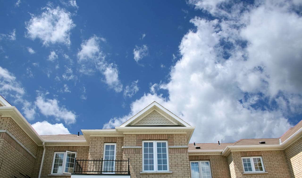 about-02 A modern brick house with large windows set against a bright blue sky with fluffy clouds.